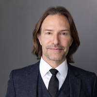 Eric Whitacre in a dark suit and tie against a gray backdrop