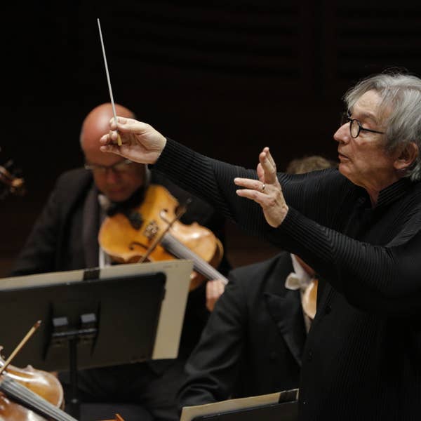 A man in a black shirt and glasses conducts an orchestra