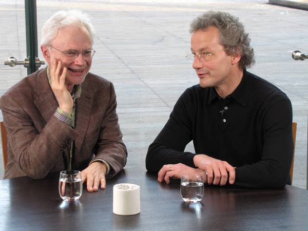 Two men talk while seated at a table.