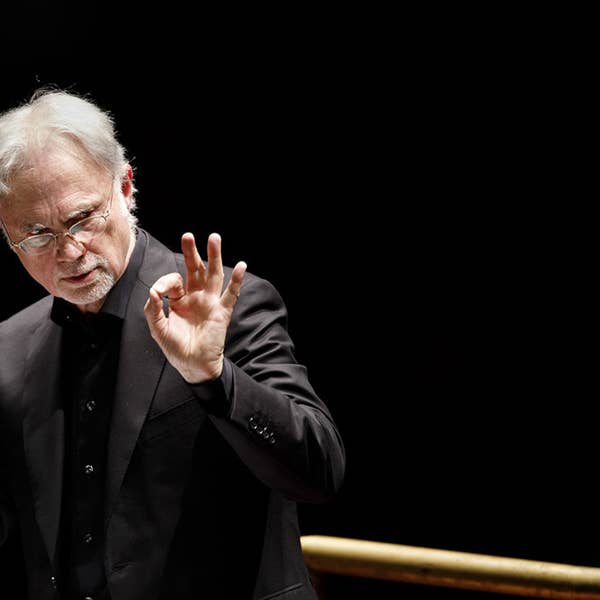 Close up of male conductor in a suit raising his hands.