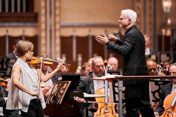 A person playing the violin stands beside a conductor.