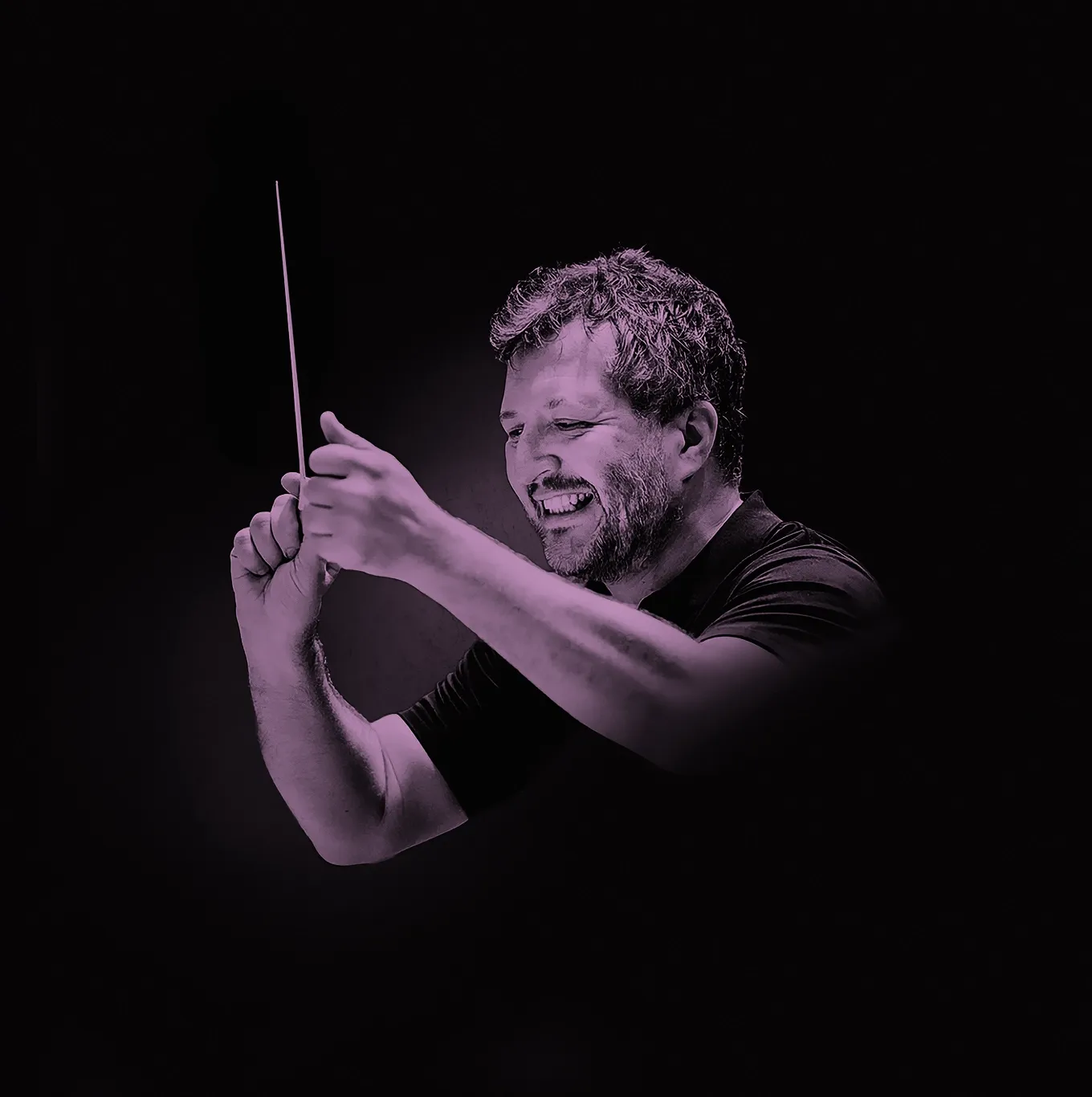 Thomas Adès smiling while conducting with a baton against a dark background.