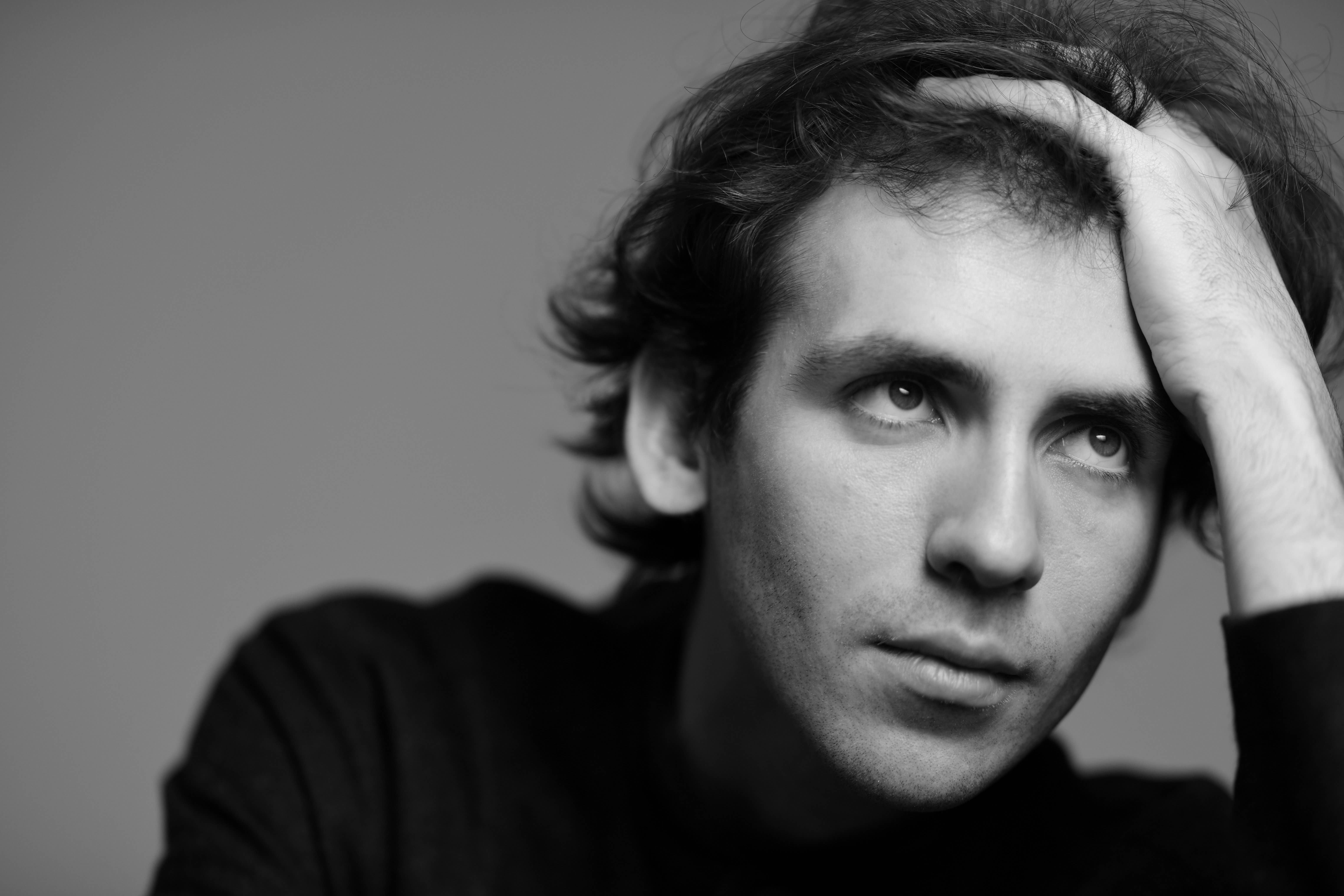 Black and white portrait of Alexandre Kantorow with hand on head, looking thoughtfully to the side.