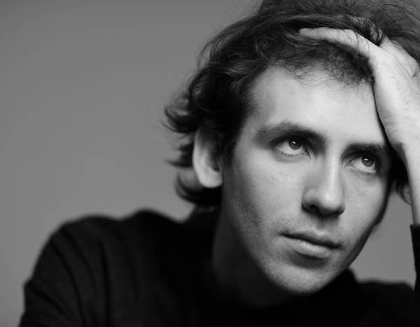 Black and white portrait of Alexandre Kantorow with hand on head, looking thoughtfully to the side.