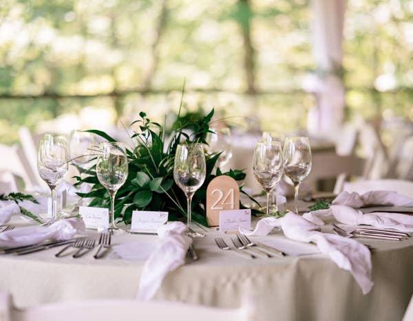 Elegant table setting with white linens, glassware, cutlery, and a green centerpiece. Table number 24 is displayed.