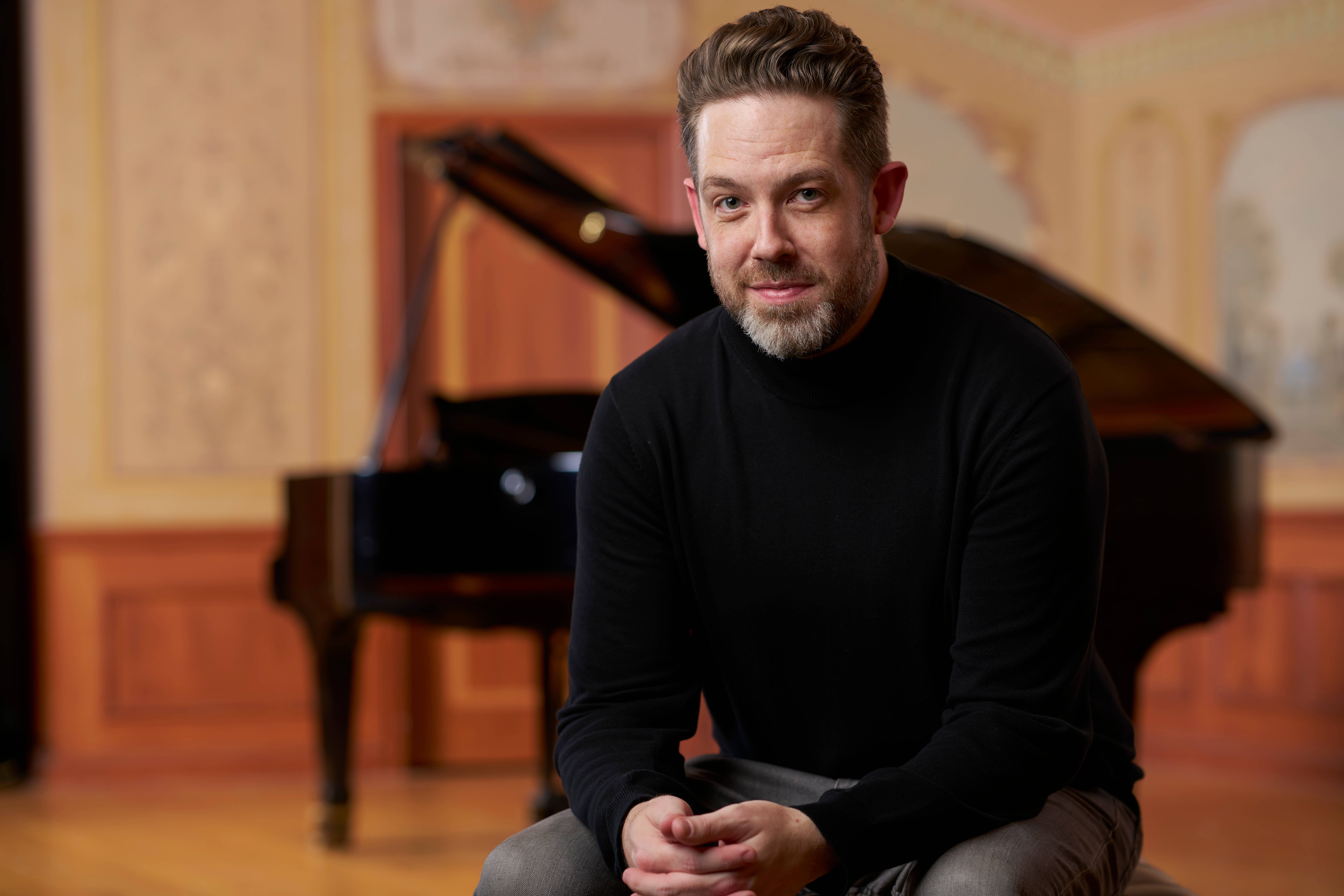 Brett Mitchell seated in front of a piano in Reinberger Chamber Hall