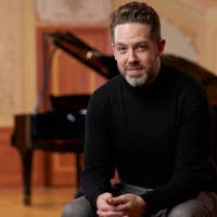 Brett Mitchell seated in front of a piano in Reinberger Chamber Hall