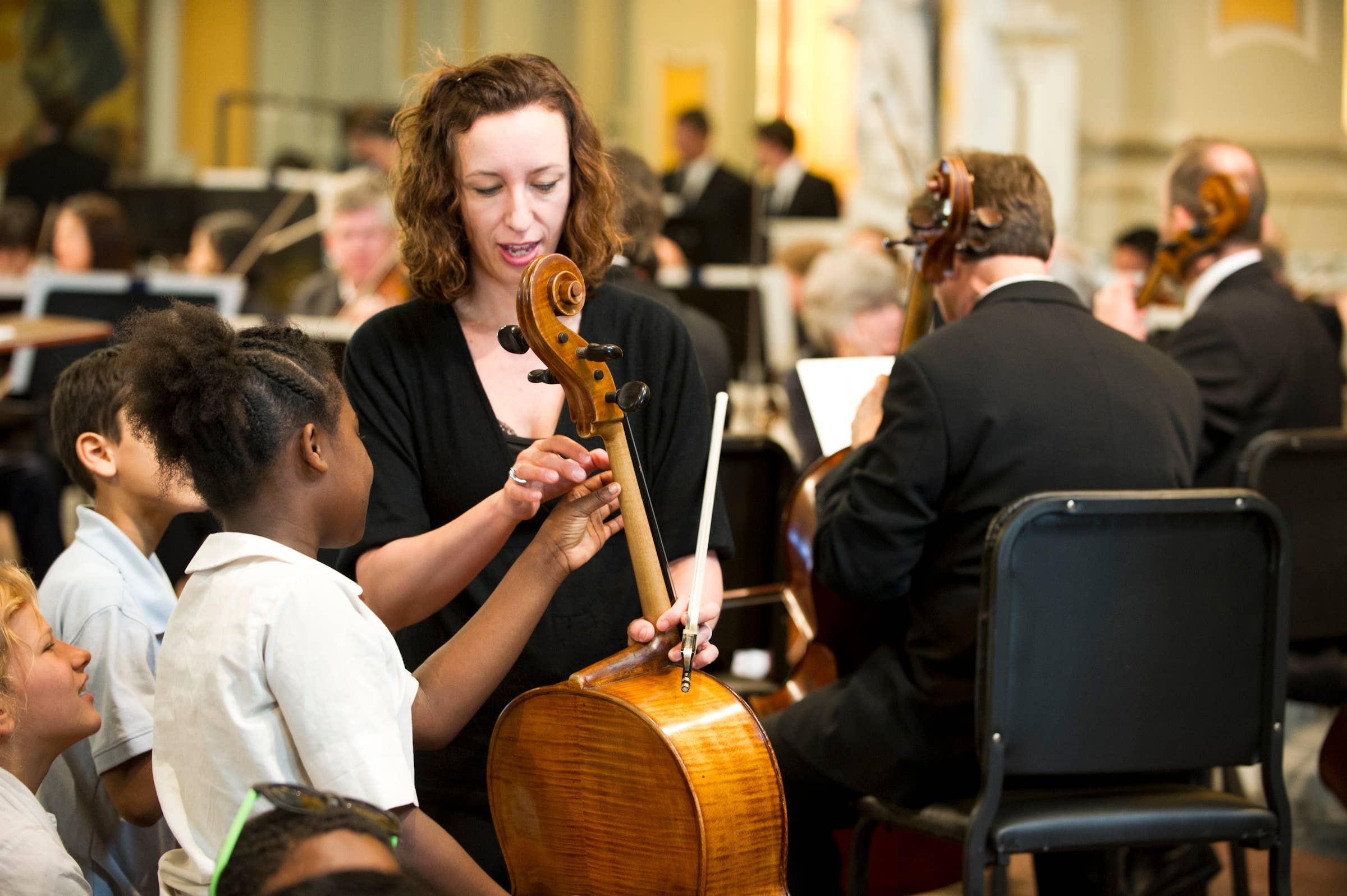 Martha Baldwin holding a cello and speaking to children at St. Coleman's church