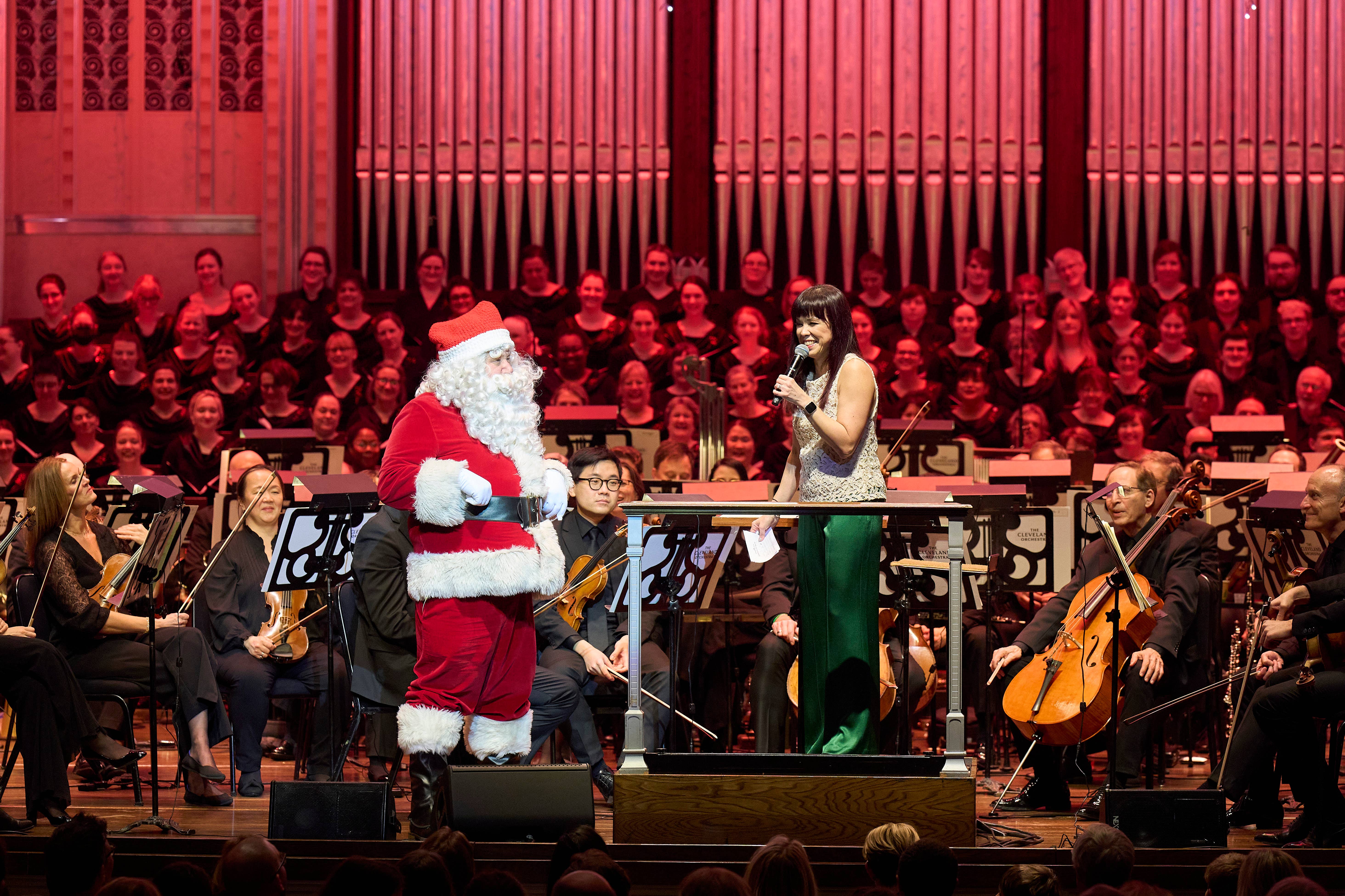 interior photo of Mandel Concert Hall with The Cleveland Orchestra on stage and Sarah Hicks talking to Santa