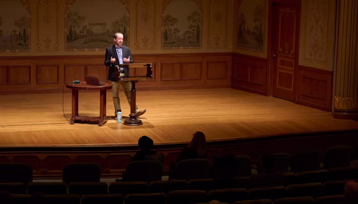 a man in a blue jacket stands on a small stage behind a podium