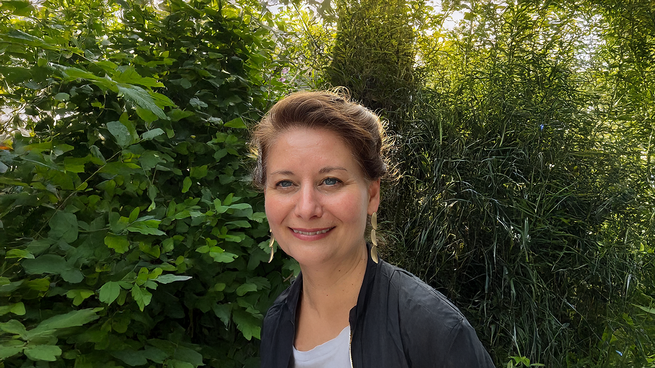 a woman in a black shirt smiles in front of greenery