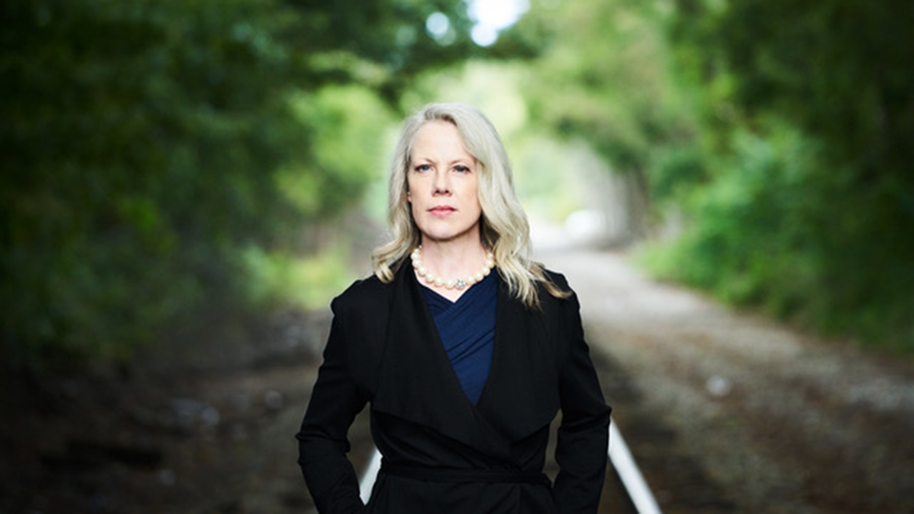 A woman stands on railroad tracks with an intense expression
