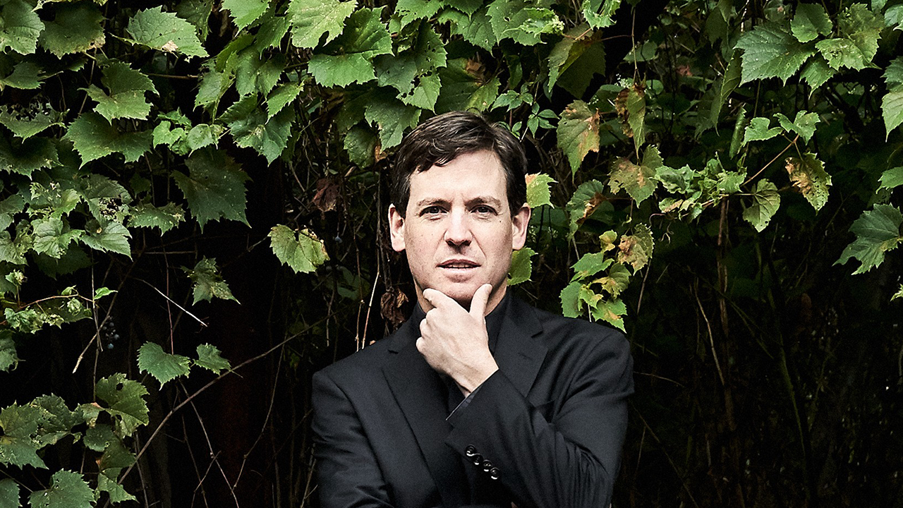 a man in a black shirt holds his chin in front of grape vines
