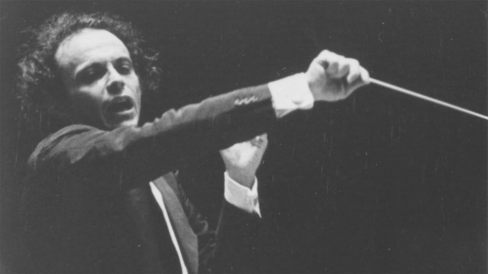 Maazel is conducting the Orchestra. His hair looks wild, and he is conducting aggressively.