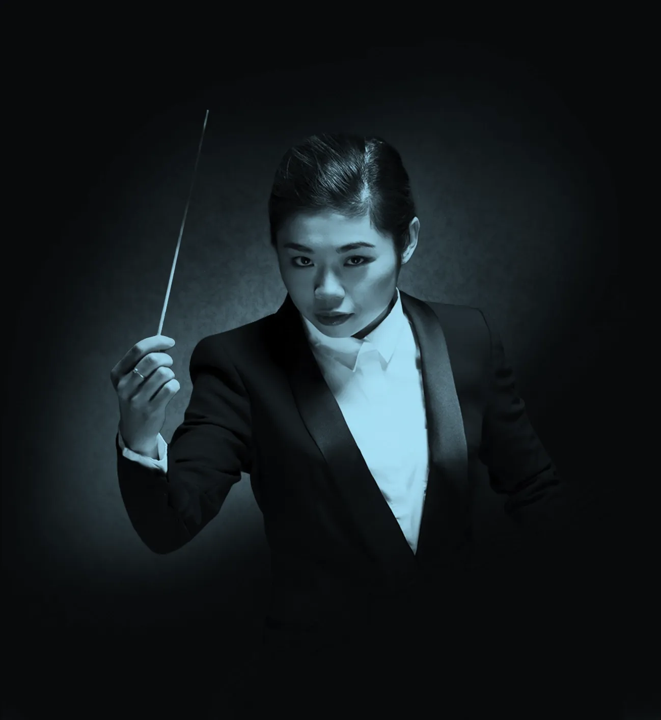 Conductor, Elim Chan, in a dark suit holding a baton, poised against a dark background with dramatic lighting.