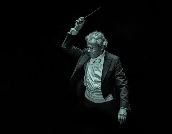 Franz Welser Möst in a tuxedo passionately leading an orchestra, baton raised, against a dark background.