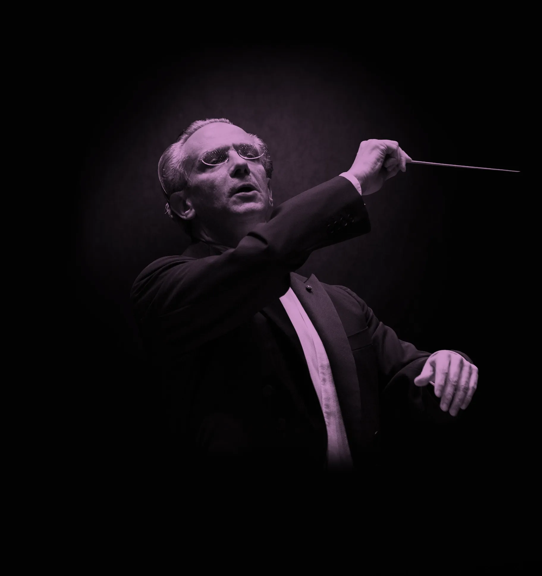 Conductor, Fabio Luisi, in a suit passionately leads an orchestra, holding a baton against a dark background.