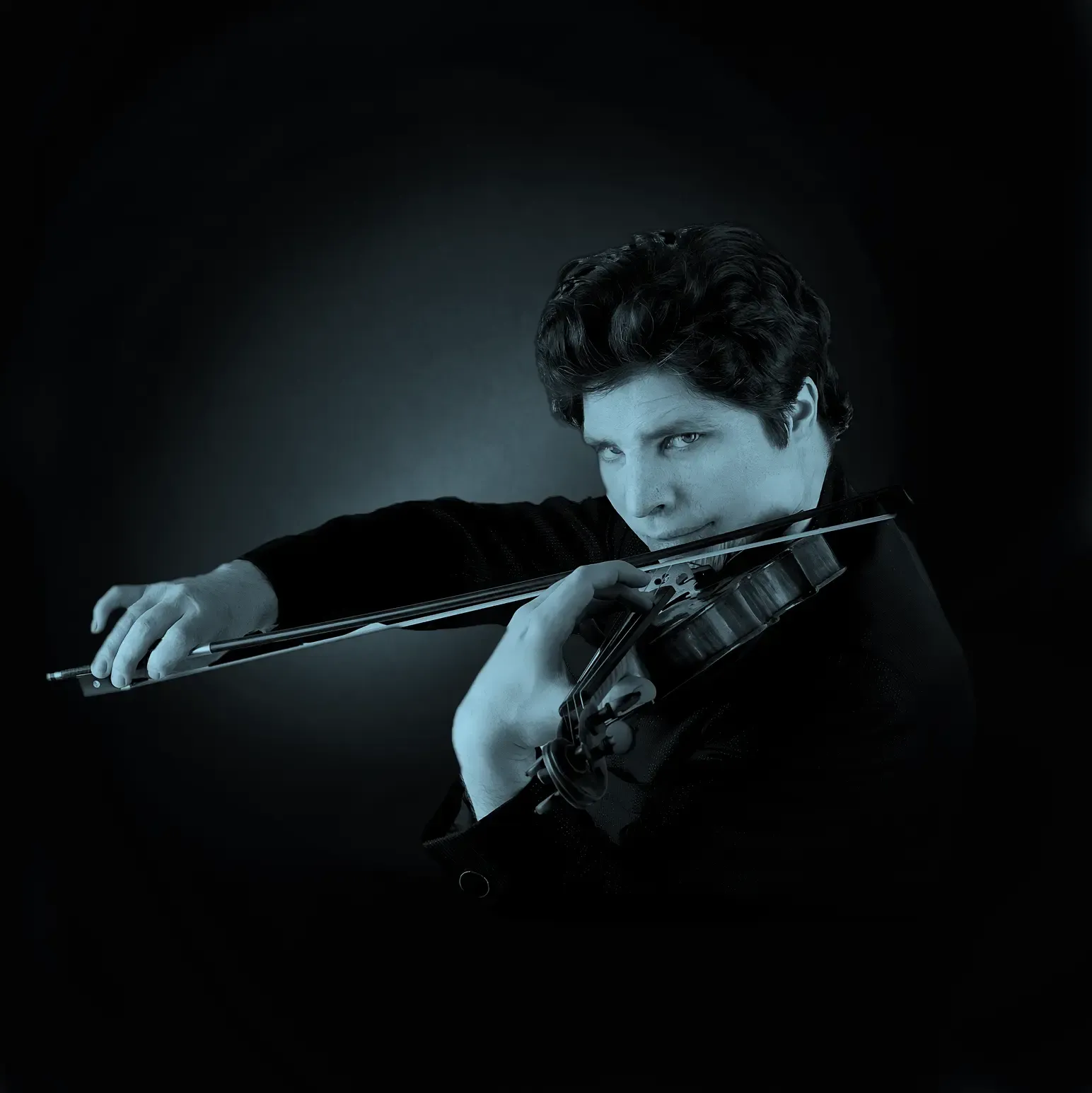 Augustin Hadelich playing a violin with intense focus, set against a dark background.