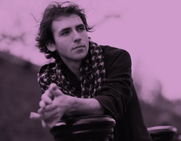 Alexandre Kantorow with tousled hair and scarf leans on a railing, gazing thoughtfully into the distance.