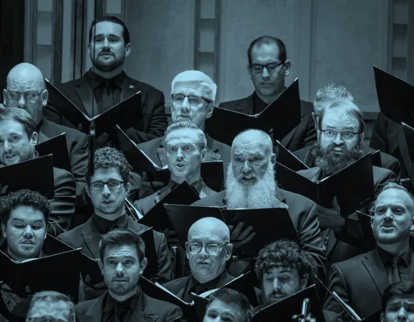 A men's choir performs, holding sheet music and wearing dark suits, with expressions of focus and intensity.