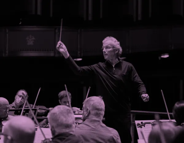Franz Welser-Möst leading The Cleveland Orchestra with raised baton, musicians focused on their instruments in rehearsal.