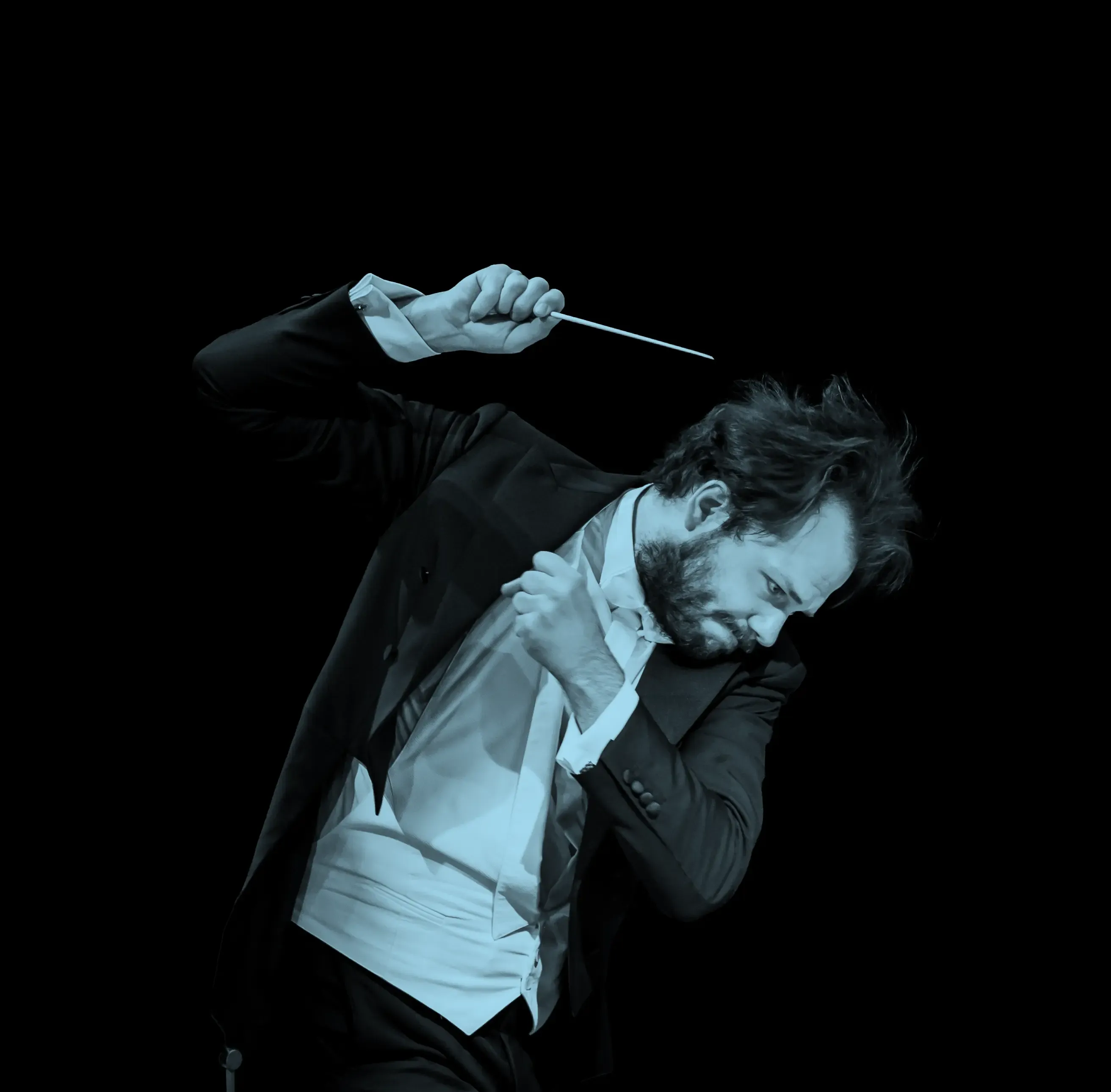 Conductor, Petr Popelka, passionately leading an orchestra, holding a baton, wearing a tuxedo, against a black background.