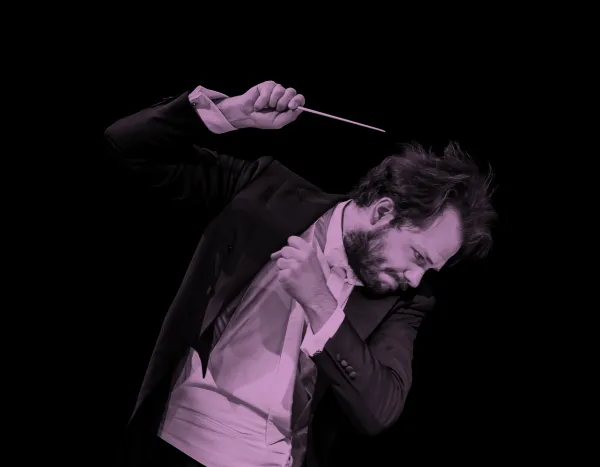 Conductor, Petr Popelka, passionately leading an orchestra, holding a baton, wearing a tuxedo, against a black background.