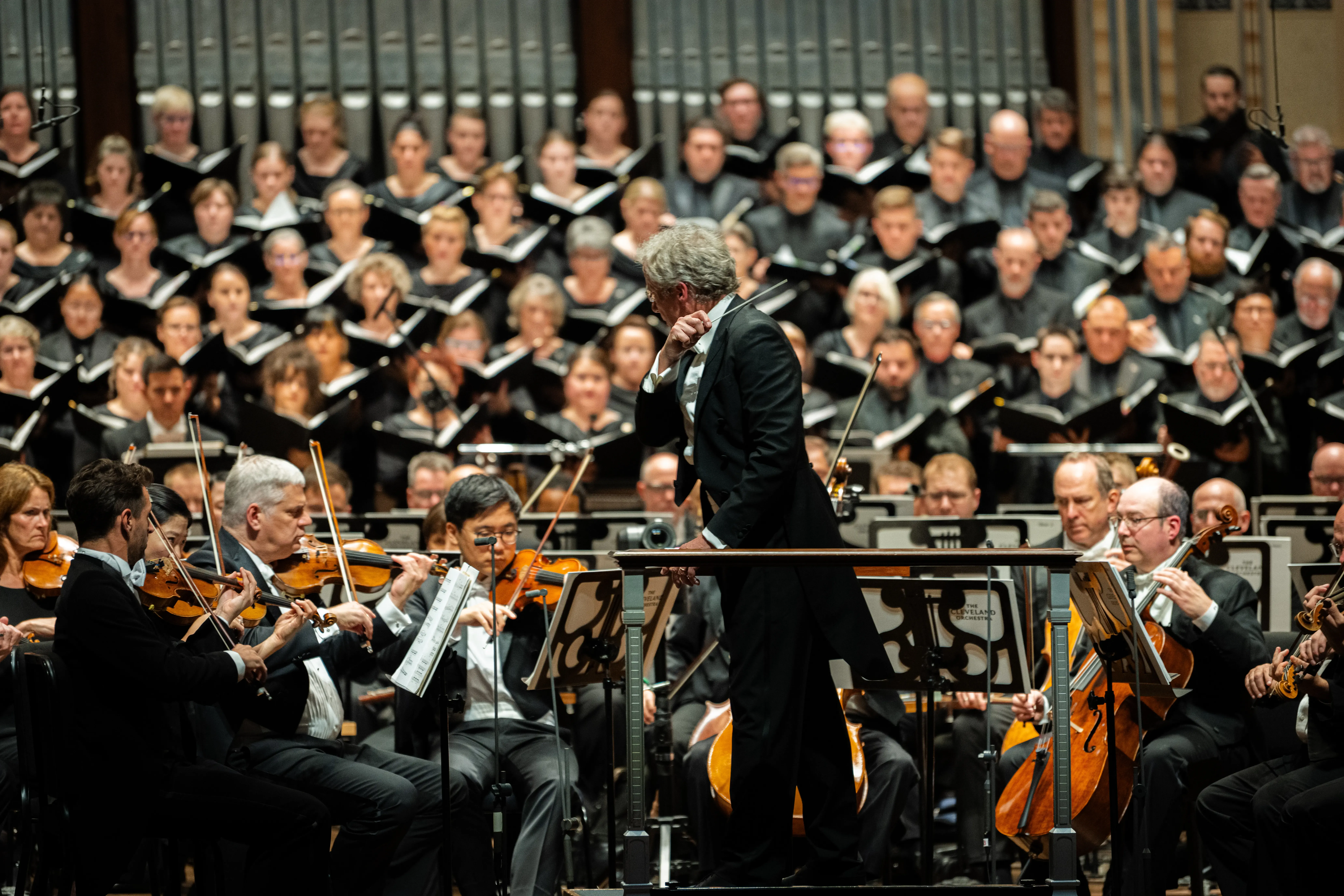 Franz Welser-Möst leading The Cleveland Orchestra with string musicians in the foreground and TCO Chorus in the background.