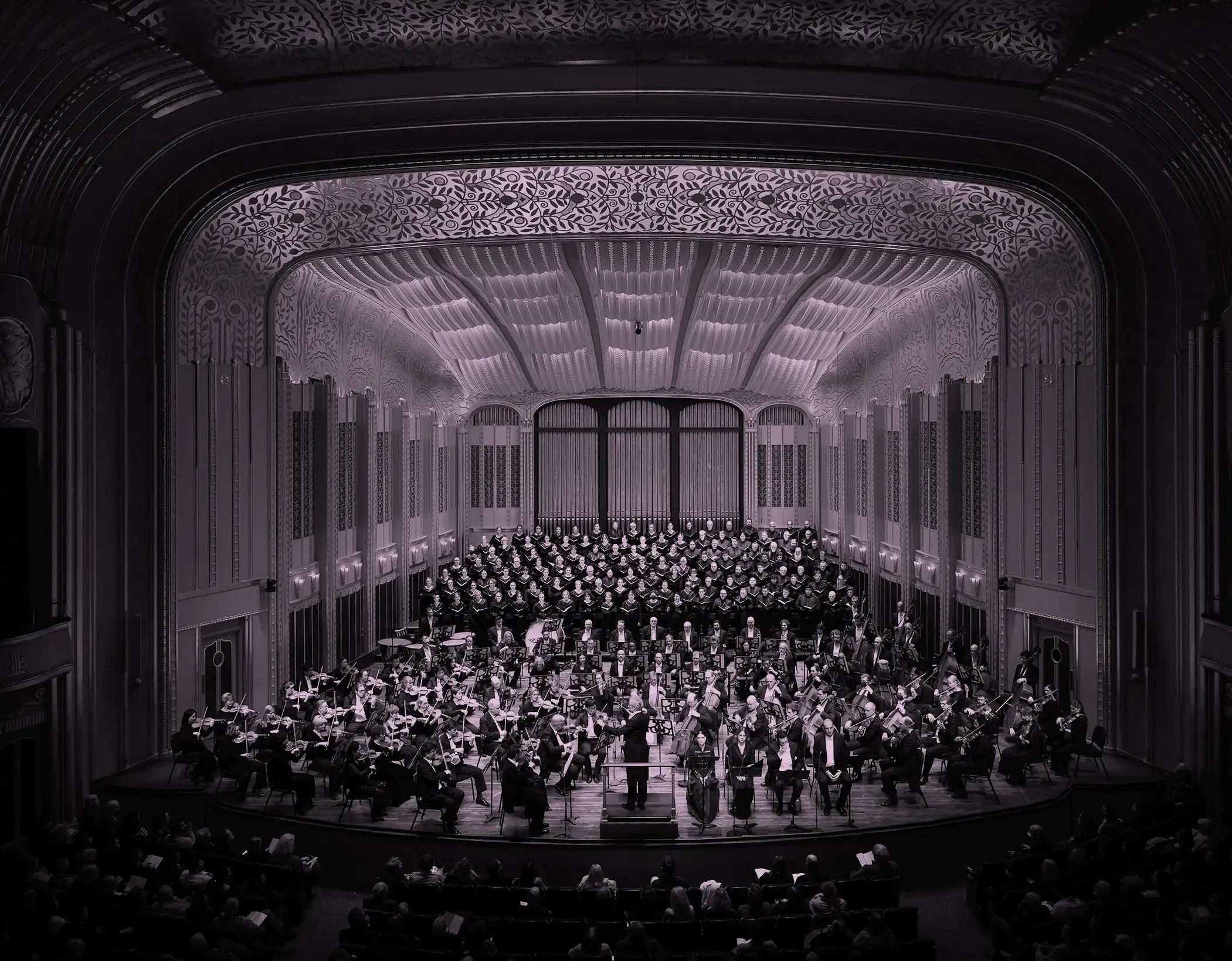 The Cleveland Orchestra and choir performing on stage in Mandel Concert Hall with ornate architectural details and a large audience.