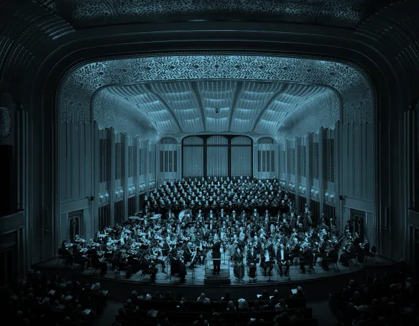 The Cleveland Orchestra and choir performing on stage in Mandel Concert Hall with ornate architectural details and a large audience.