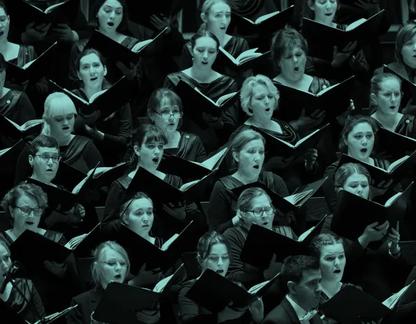 Choir members in dark attire singing with open sheet music, expressions focused and engaged.