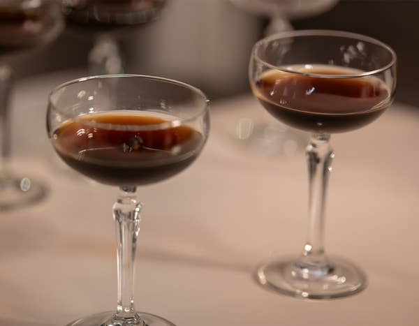 Close-up of a stemmed glass with amber-red wine, background blurred with a person serving another drink