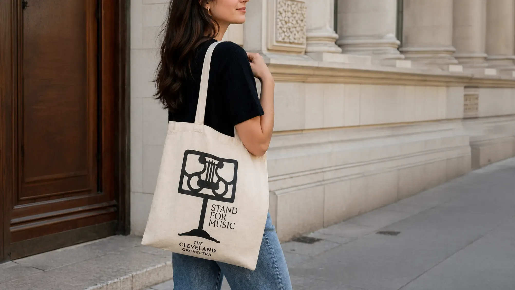 Woman holding a tote bag reading “Stand for Music” with a city building facade in the background.