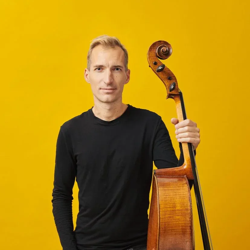 Stephan Koncz posing against a bright yellow backdrop with a bass