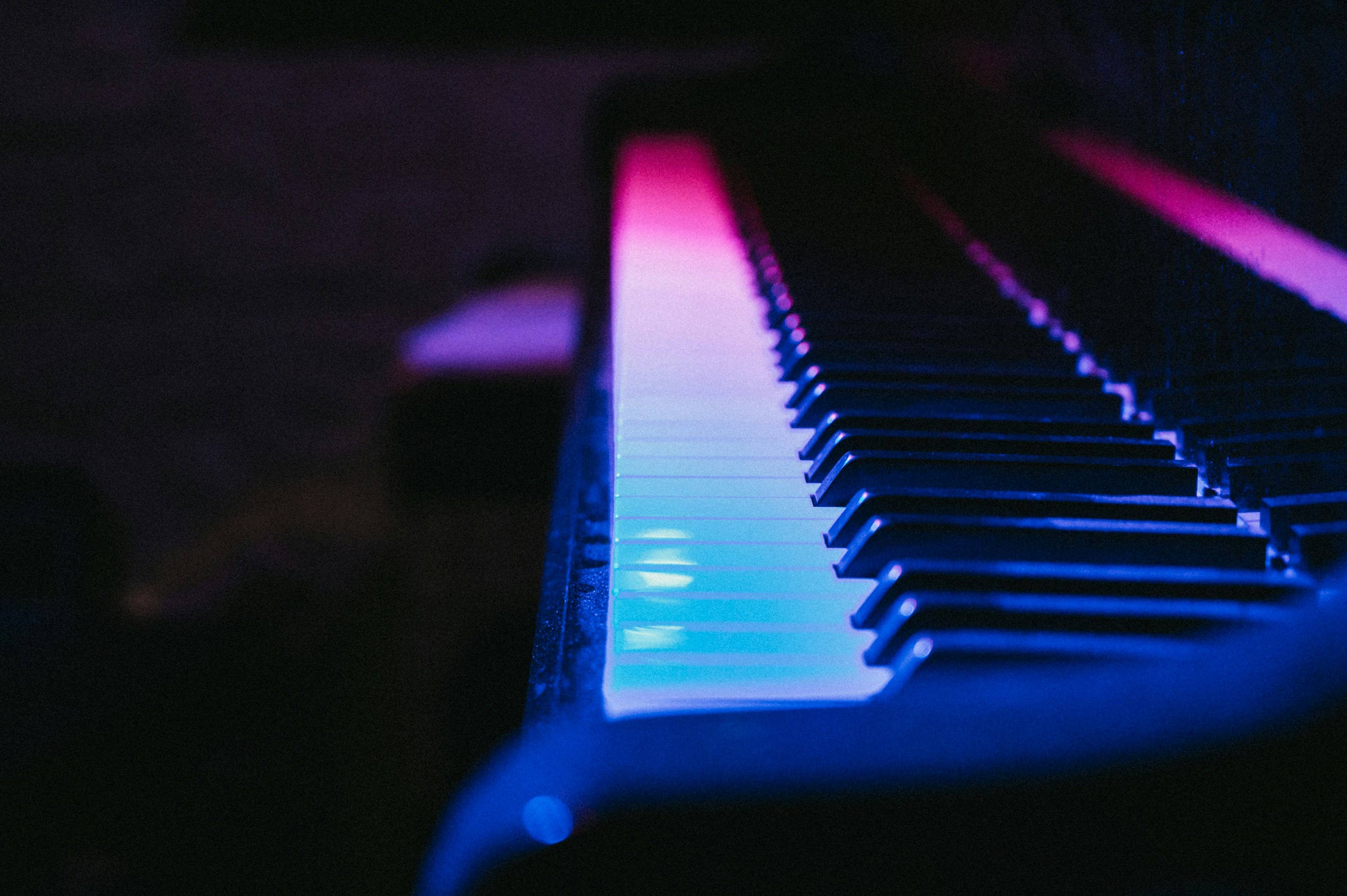 Close-up of piano keys illuminated by pink and blue lighting in a dark setting.