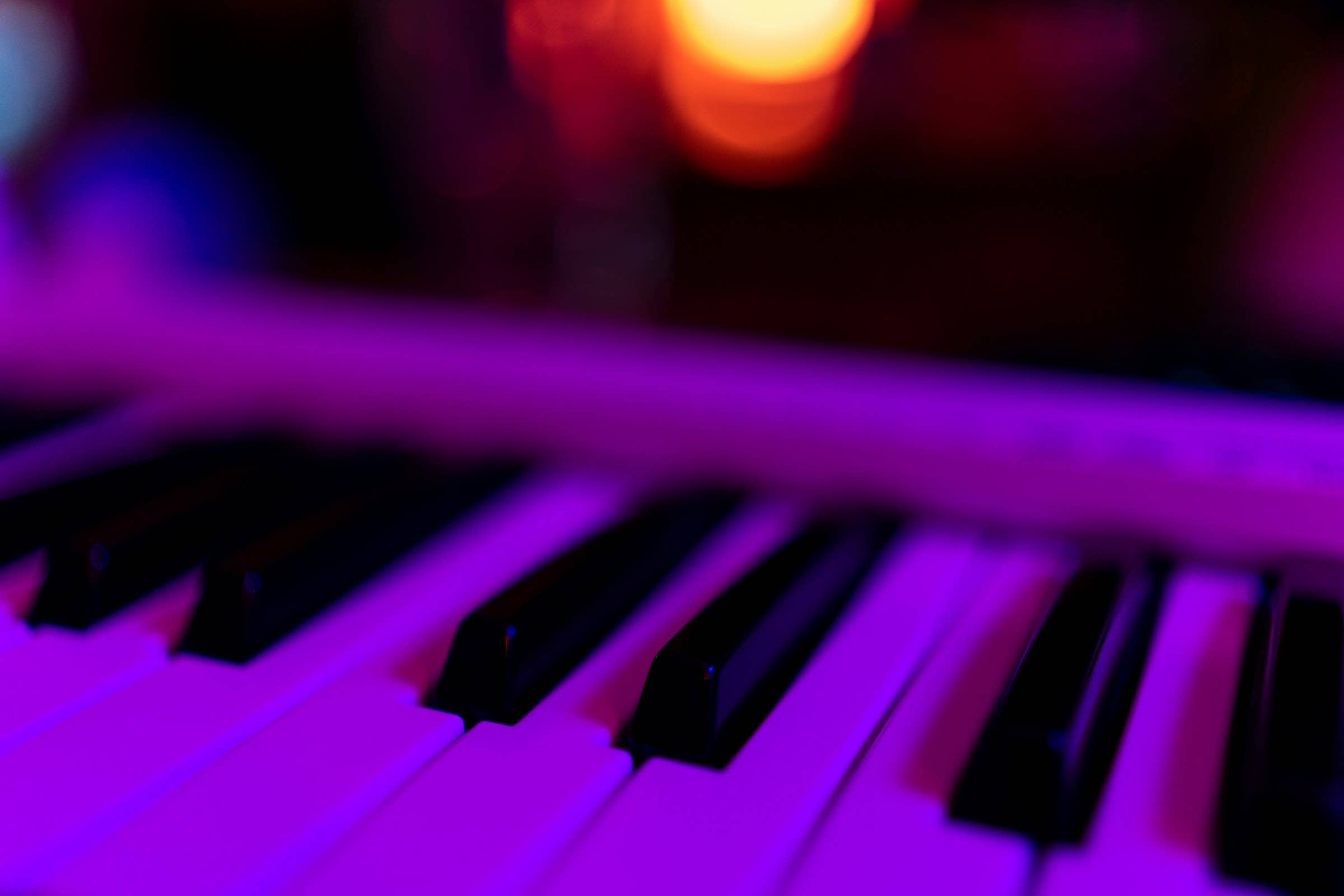 Close-up of piano keys illuminated by purple and orange lighting, creating a vibrant and moody atmosphere.