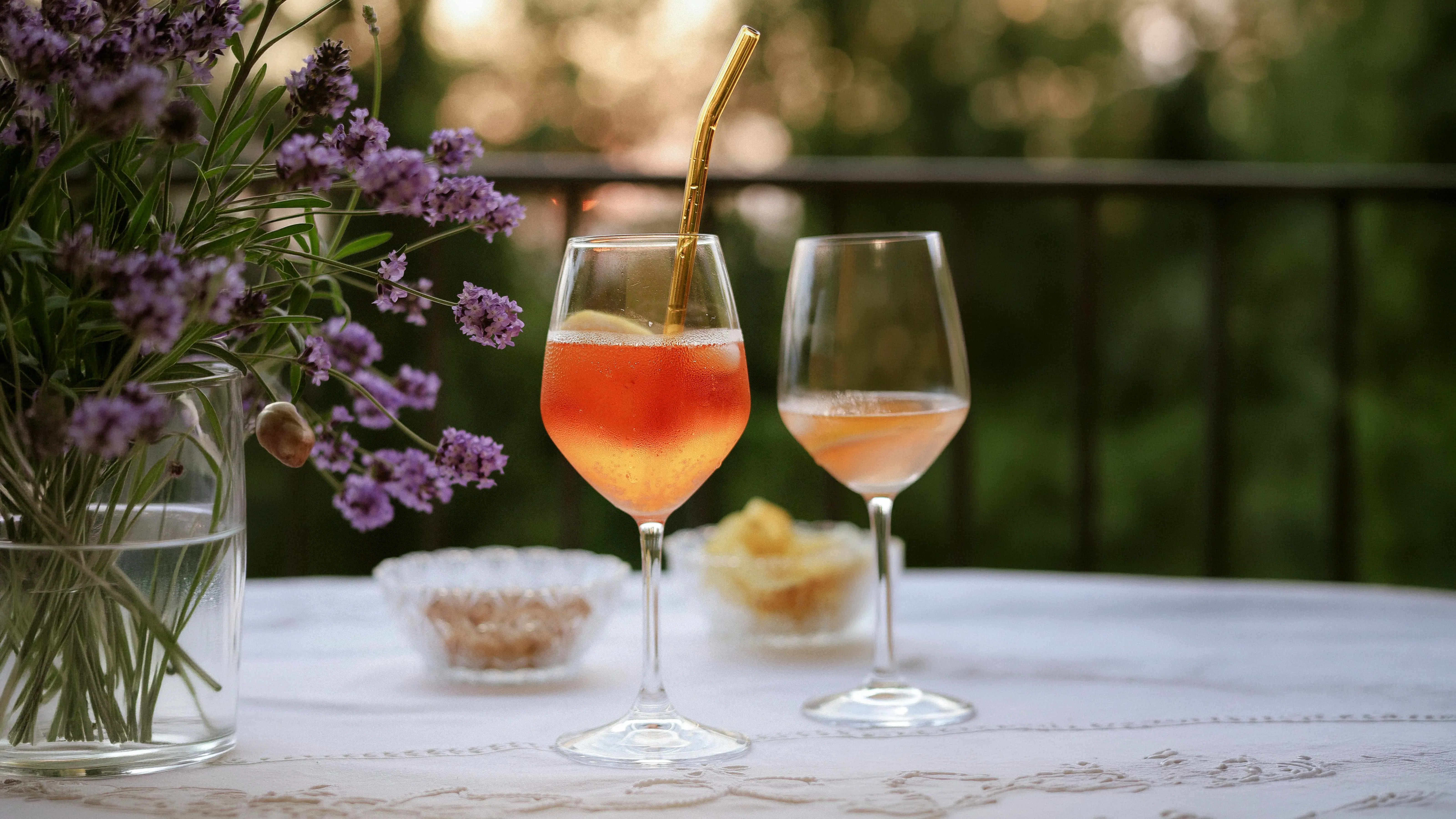 Golden cocktail in a stemmed glass with an amber drink, purple flowers, and a garden patio background.