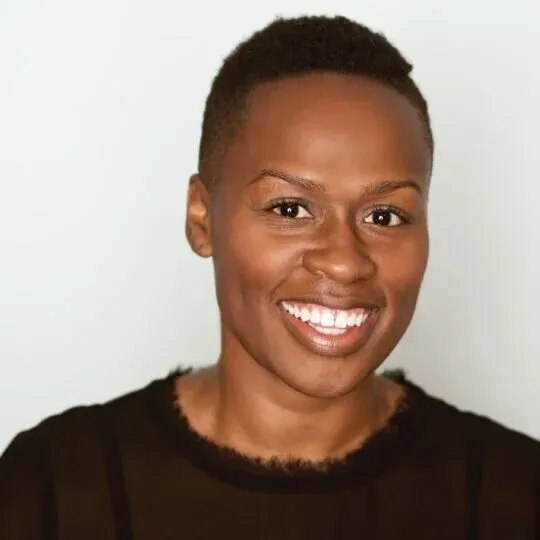 Smiling portrait of a young Black person with short hair against a plain light background