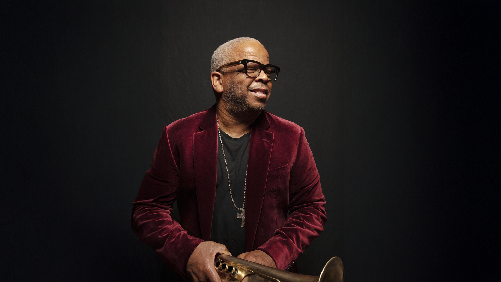 Terence Blanchard in a red jacket holding a trumpet in font of a dark gray backdrop