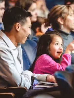 Young child points to the stage next to parent seated in Mandel Hall