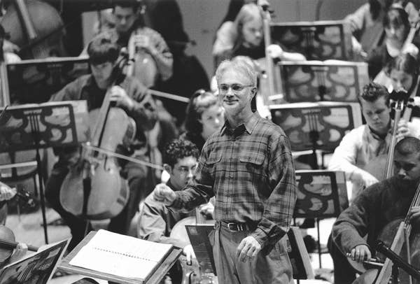 A conductor standing in front of a group of young people playing instruments.
