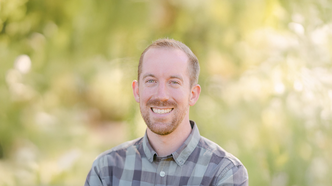 a man in a plaid shirt poses outdoors
