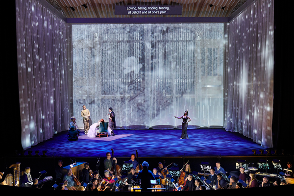 Four actors stand on a stage covered with stary light projections.