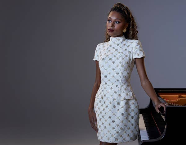Isata Kanneh-Mason standing by a piano in a white dress
