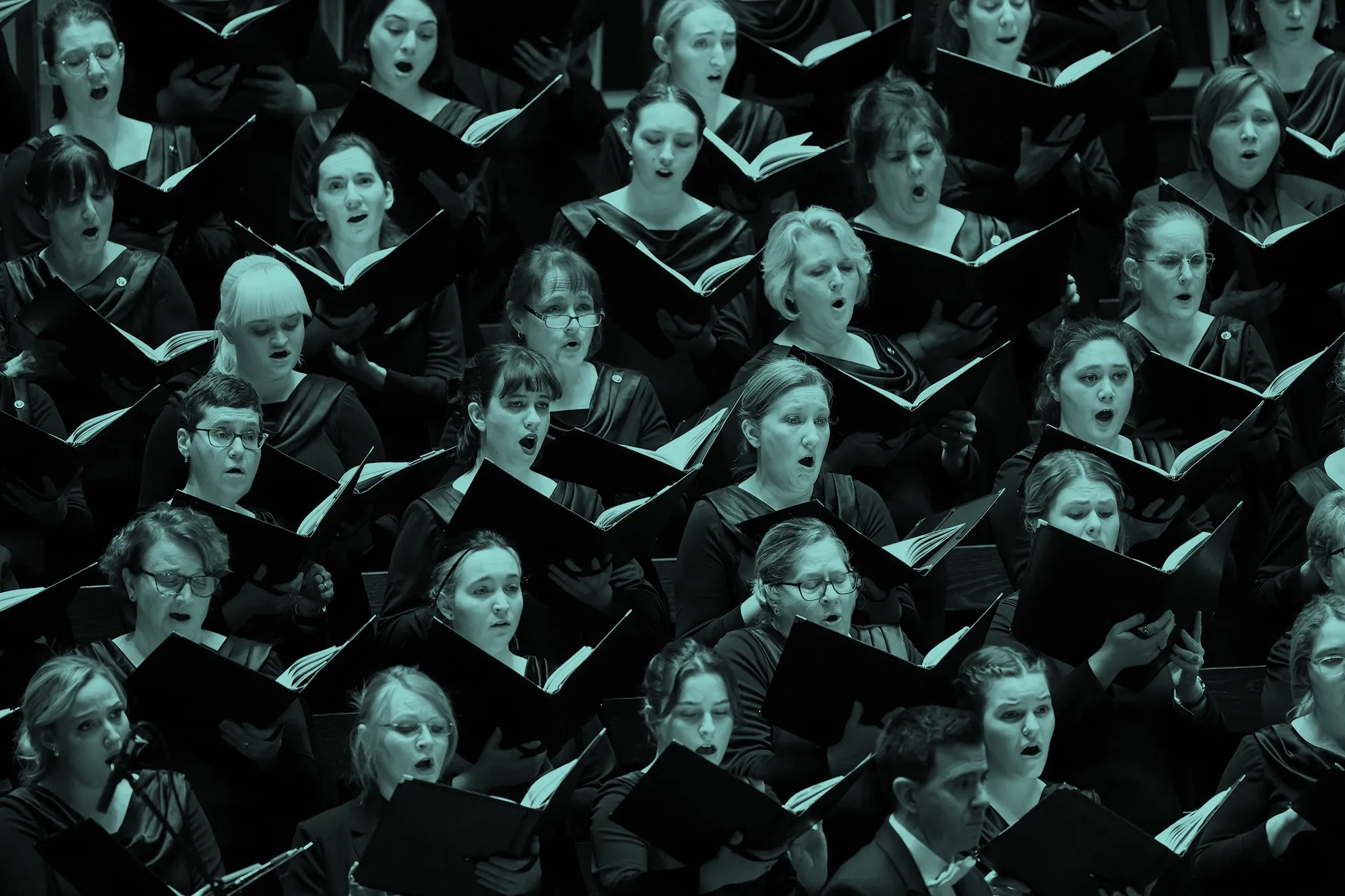 Choir members in dark attire singing with open sheet music, expressions focused and engaged.