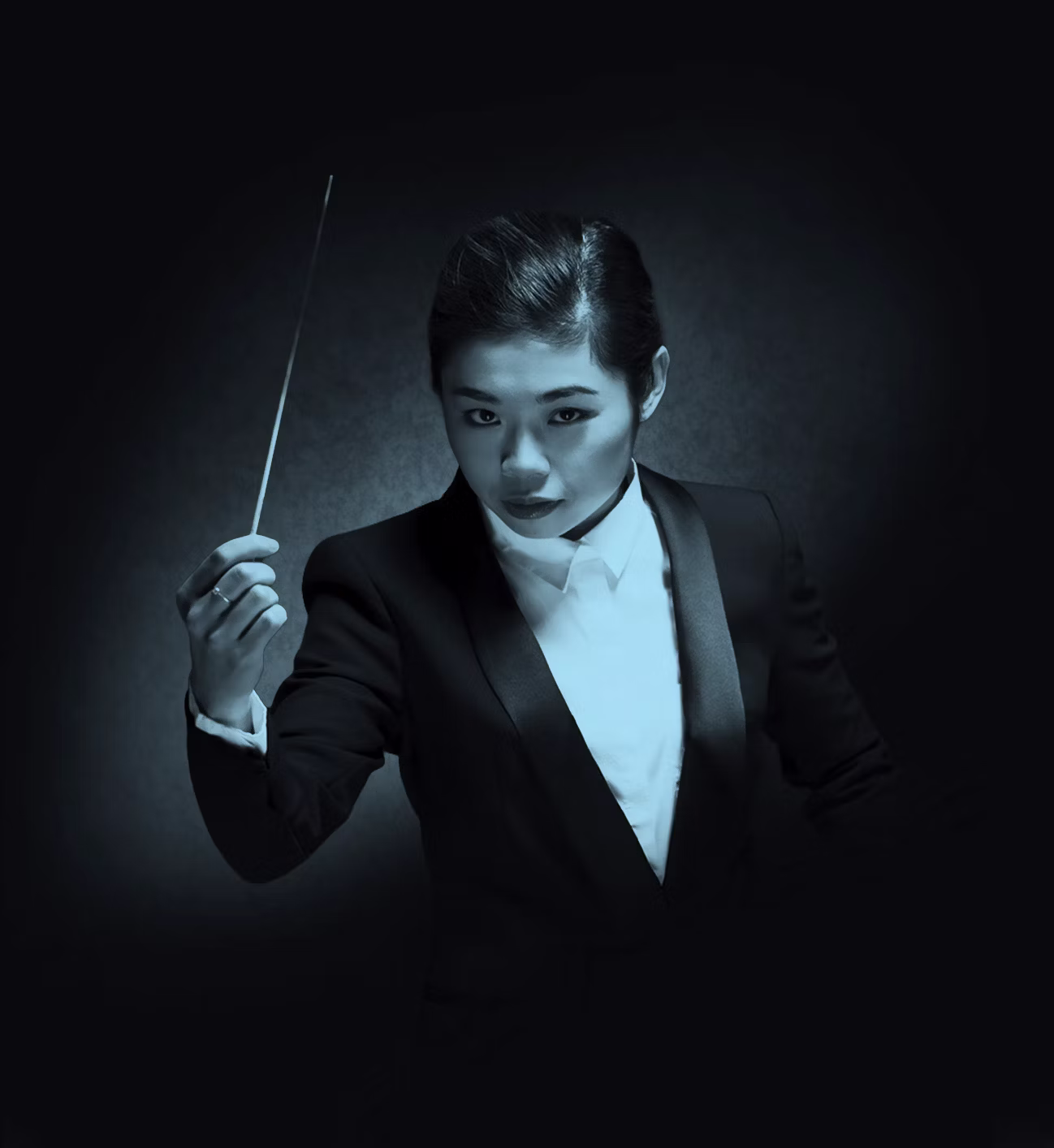 Conductor, Elim Chan, in a dark suit holding a baton, poised against a dark background with dramatic lighting.
