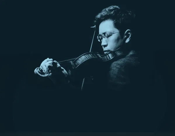 Paul Huang with glasses plays violin in dramatic blue light, holding the bow mid-performance against a dark background.