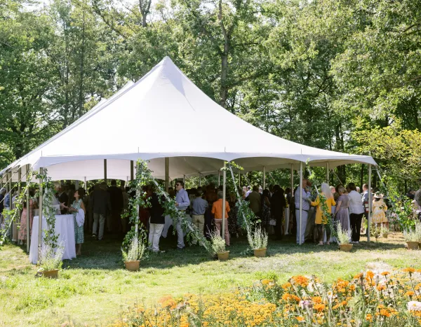 Guests mingle under a white event tent at a garden wedding, surrounded by greenery and potted flowers