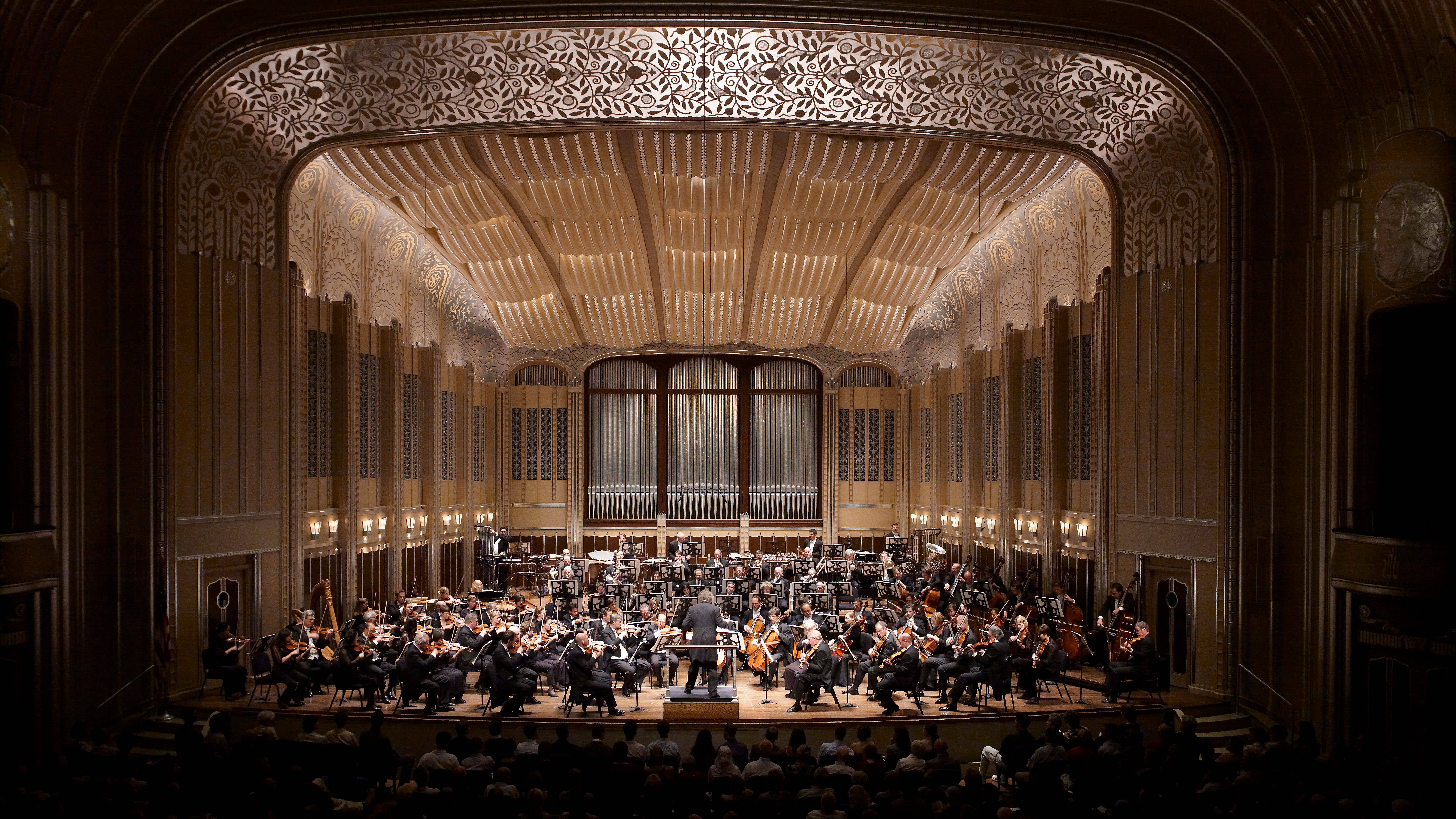 The Cleveland Orchestra, conducted by Franz Welser-Möst, is performing in Severance Hall. The photo shows the Orchestra and Franz animatedly performing and conducting, respectively. 