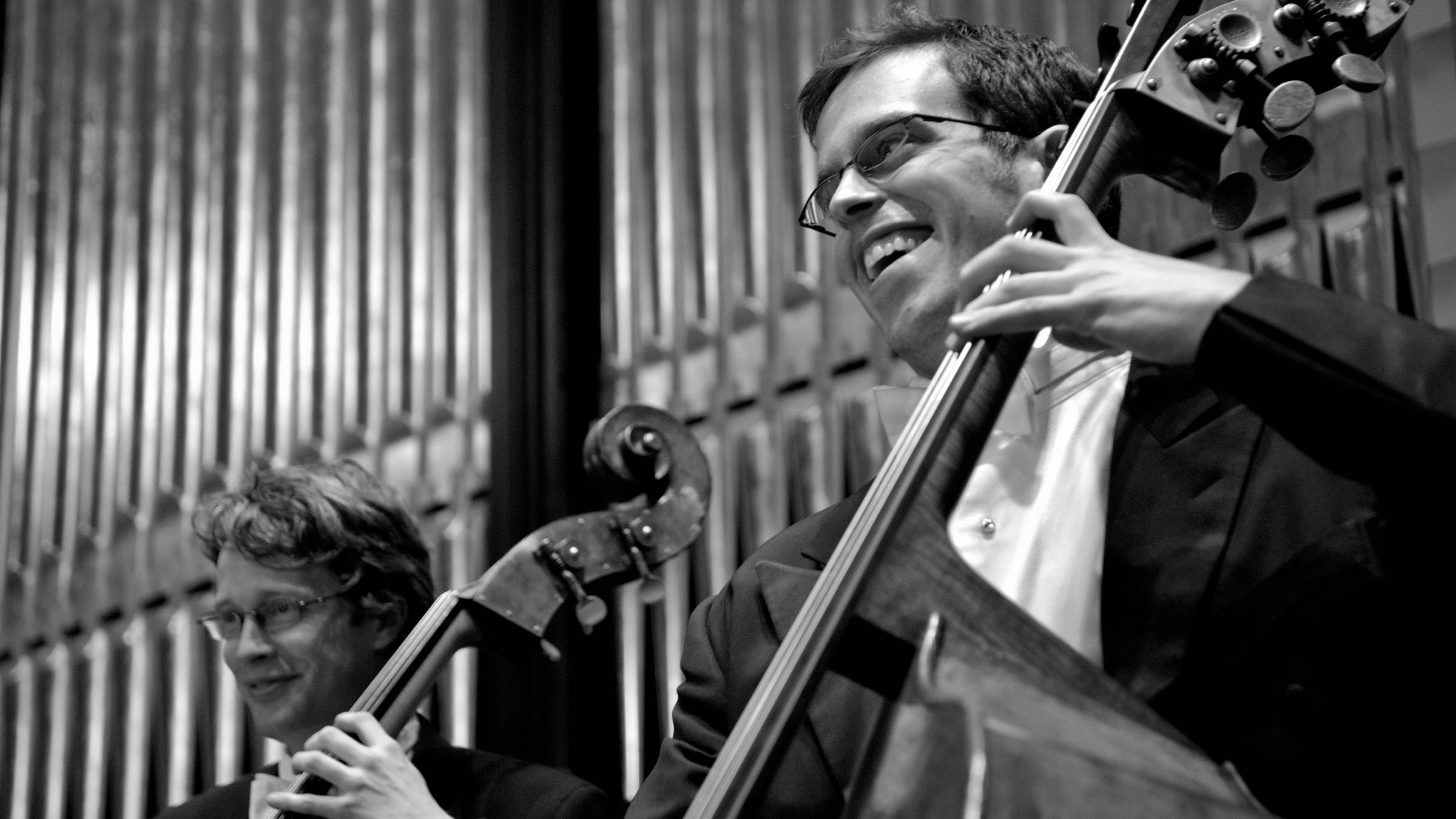 Two musicians playing the bass and smiling broadly.
